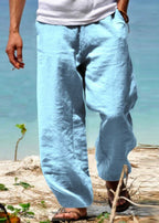 Homme portant un pantalon en lin bleu clair sur une plage, style décontracté estival, mode masculine bord de mer, confort et élégance.