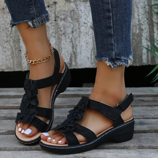 Sandales noires à talons compensés avec fleurs, portées avec un jean déchiré et bracelet chaîne doré. Mode féminine, chaussures été élégantes.