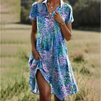 Robe d'été fleurie bleue et violette, manches courtes, col en V, portée par une femme dans un champ. Mode féminine, style décontracté.