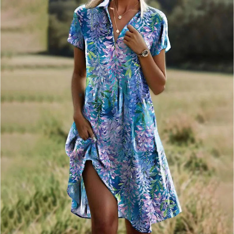 Robe d'été fleurie bleue et violette, manches courtes, col en V, portée par une femme dans un champ. Mode féminine, style décontracté.