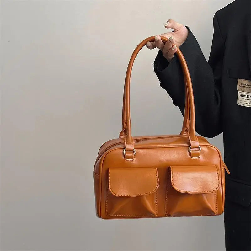 Sac à main en cuir marron avec deux poches avant, porté par une personne en veste noire. Accessoire mode élégant et tendance.