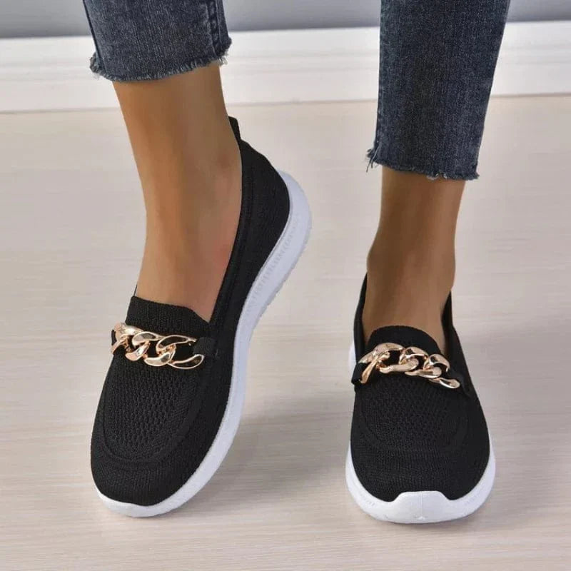 Chaussures mocassins noirs pour femme avec chaîne dorée, semelle blanche, portées avec un jean. Mode féminine, chaussures tendance, confortables.