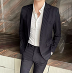 Homme en costume rayé noir et chemise blanche, posant contre un mur en marbre. Mode masculine élégante, tenue professionnelle, style moderne.