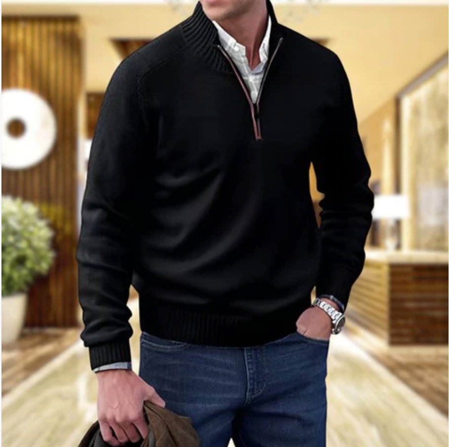 Homme portant un pull noir à col zippé, chemise blanche et jean bleu, tenant une veste marron. Mode masculine élégante et décontractée.