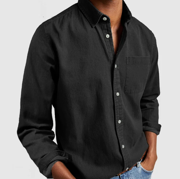 Homme portant une chemise noire en denim, manches longues, avec poches, sur fond blanc. Mode masculine, style décontracté, tendance actuelle.