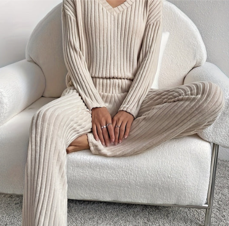 Femme assise sur un canapé blanc, portant un ensemble en tricot beige côtelé. Mode automne-hiver, confort et élégance, tenue décontractée.
