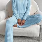Femme assise sur un fauteuil blanc, portant un ensemble bleu côtelé confortable. Mode détente, tenue cosy, intérieur moderne.