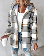 Femme portant une chemise à carreaux gris et blanc avec capuche, tenue décontractée, jeans déchirés, tenant un gobelet blanc. Mode automne tendance.
