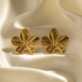 Boucles d'oreilles en forme de fleur dorée sur tissu satiné. Bijoux élégants, accessoires mode, design floral, tendance féminine.
