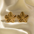 Boucles d'oreilles en forme de fleur dorée sur tissu satiné. Bijoux élégants, accessoires mode, design floral, tendance féminine.