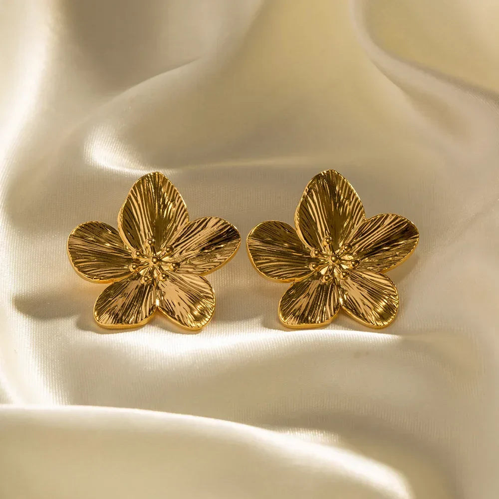 Boucles d'oreilles en forme de fleur dorée sur tissu satiné. Bijoux élégants, accessoires mode, design floral, tendance féminine.