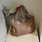 Sac à main en cuir marron avec poignées robustes, posé sur une surface beige. Élégant et spacieux, idéal pour un usage quotidien ou professionnel.