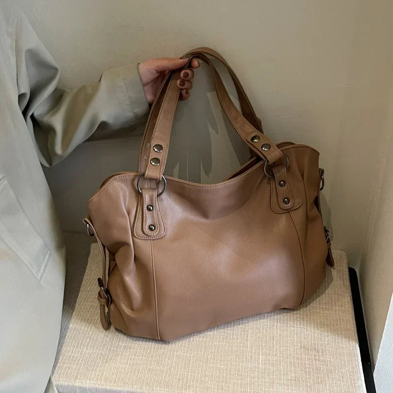Sac à main en cuir marron avec poignées robustes, posé sur une surface beige. Élégant et spacieux, idéal pour un usage quotidien ou professionnel.