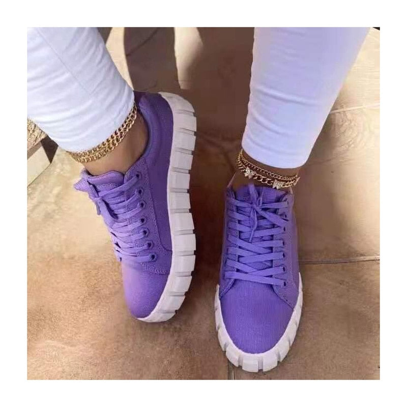 Chaussures violettes tendance avec semelles épaisses blanches, portées avec un pantalon blanc et bracelets de cheville dorés. Mode urbaine féminine.