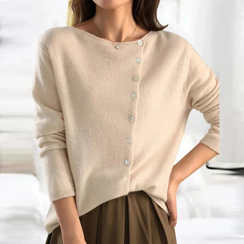 Femme portant un pull beige asymétrique à boutons, manches longues, col bateau, style décontracté. Mode automne-hiver élégante et tendance.