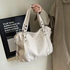 Sac à main en cuir blanc élégant avec poignées robustes, porté par une personne en manteau beige. Accessoire mode chic, tendance et polyvalent.