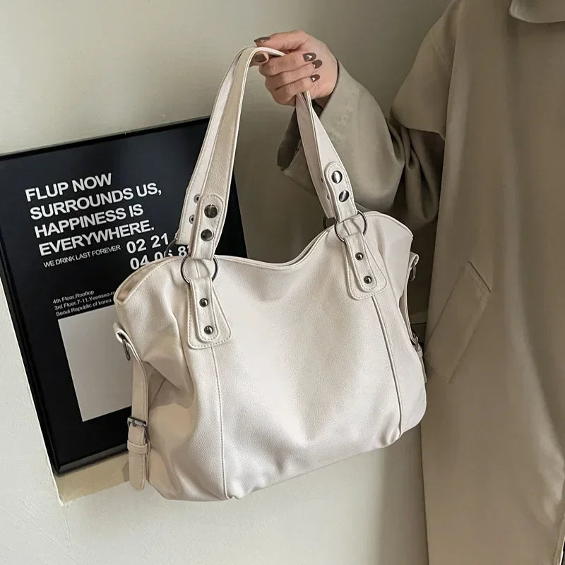 Sac à main en cuir blanc élégant avec poignées robustes, porté par une personne en manteau beige. Accessoire mode chic, tendance et polyvalent.