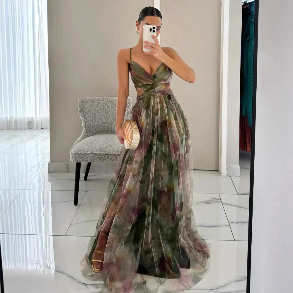 Femme en robe longue à motifs floraux, tenant un sac à main doré, se prenant en photo dans un miroir. Mode élégante, tenue de soirée chic.