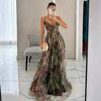 Femme en robe longue à motifs floraux, tenant un sac à main doré, se prenant en photo dans un miroir. Mode élégante, tenue de soirée chic.
