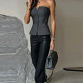 Femme en top bustier gris et pantalon noir, tenant un sac à main noir. Mode élégante, tenue chic, style moderne.