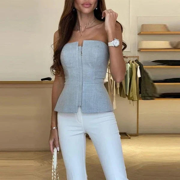 Femme portant un haut bustier gris élégant et un pantalon blanc, montre-bracelet argentée, dans une boutique de mode moderne. Style chic et tendance.