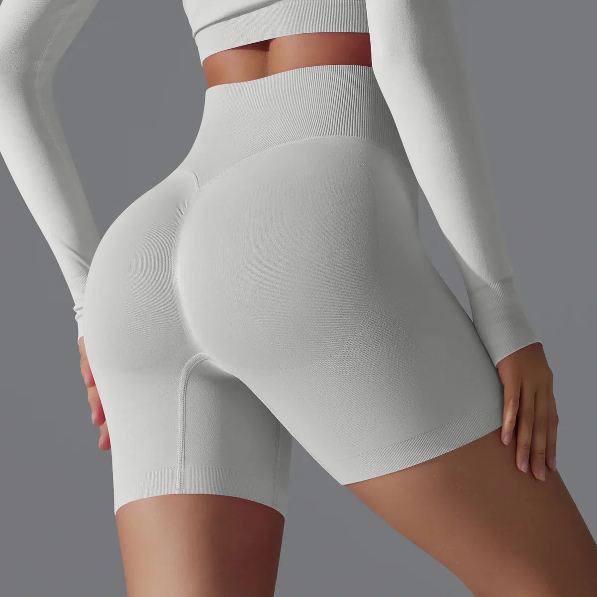 Dame en tenue de sport blanche moulante, vue de dos, mettant en valeur des shorts de fitness taille haute. Mode active, vêtements de sport élégants.