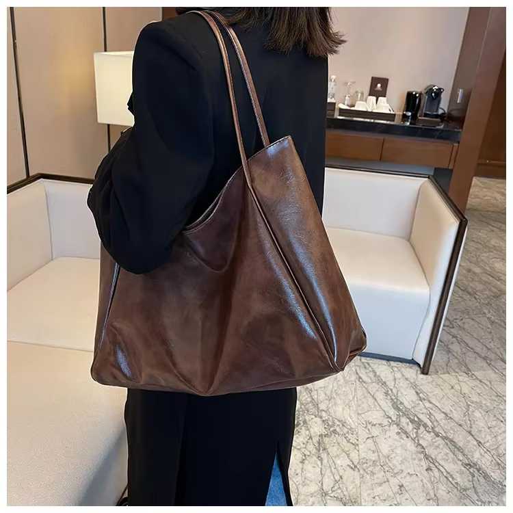 Sac à main en cuir marron porté par une femme en manteau noir dans un salon moderne. Accessoire mode élégant, tendance et pratique.