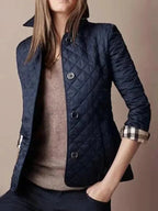 Femme portant une veste matelassée bleu marine élégante, manches retroussées, sur un pull beige. Mode automne chic et tendance.