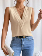 Femme portant un haut beige sans manches avec col en V, collier doré, jean bleu et sac blanc. Mode élégante, tenue chic, accessoires tendance.