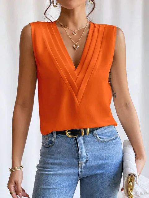 Femme portant un haut orange sans manches avec col en V, jeans bleu clair, ceinture noire, bijoux dorés, et sac blanc. Mode élégante et tendance.