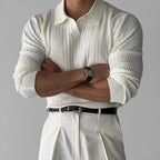 Homme en pull blanc côtelé, manches retroussées, montre noire, pantalon blanc plissé, ceinture noire. Mode élégante et minimaliste.