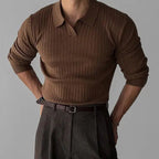 Homme portant un pull marron côtelé à col polo, manches retroussées, avec un pantalon gris foncé. Mode masculine élégante et décontractée.