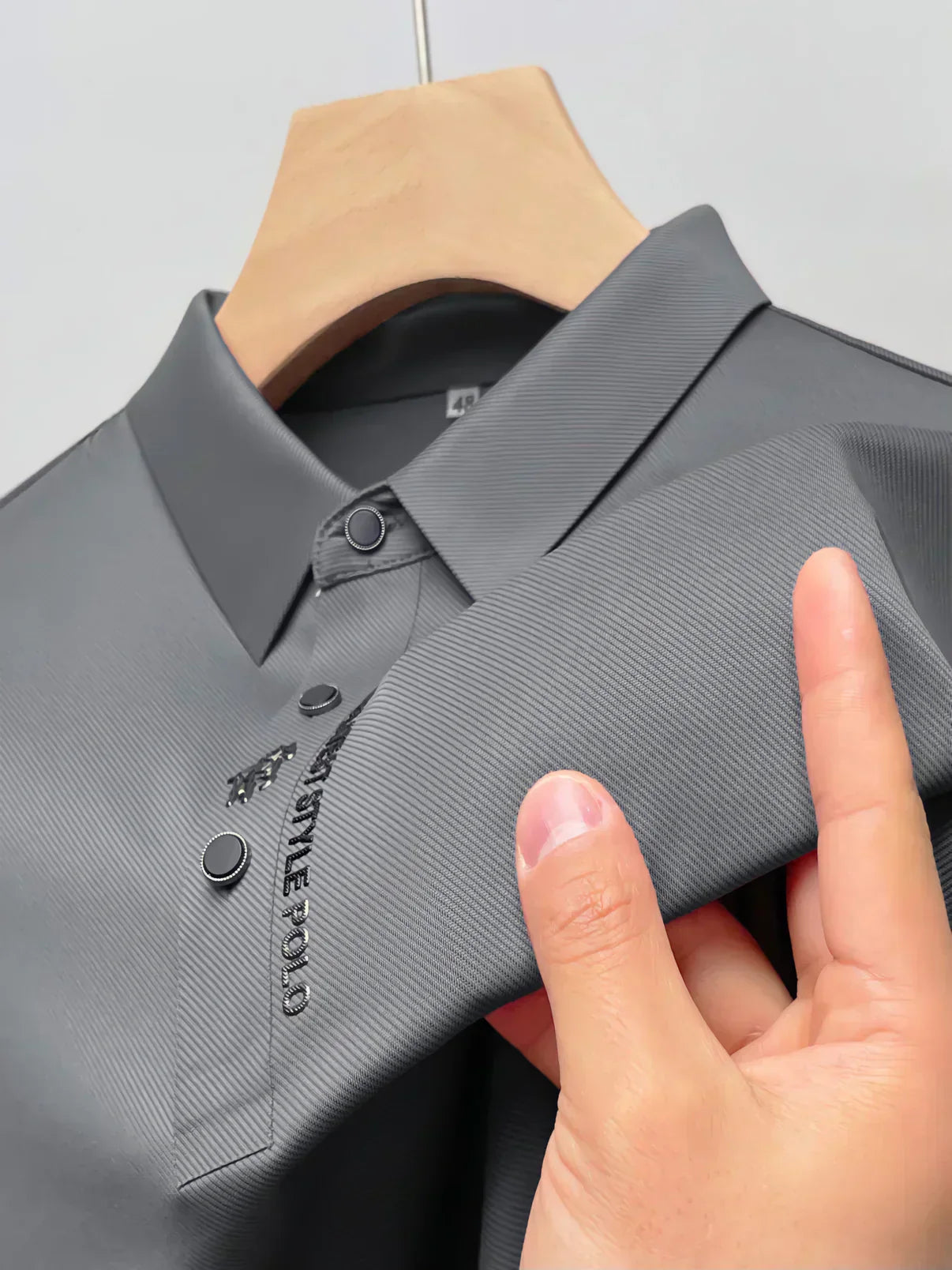 Chemise polo grise élégante sur cintre, tissu texturé, boutons noirs, logo brodé, mode masculine, vêtement tendance, style décontracté chic.