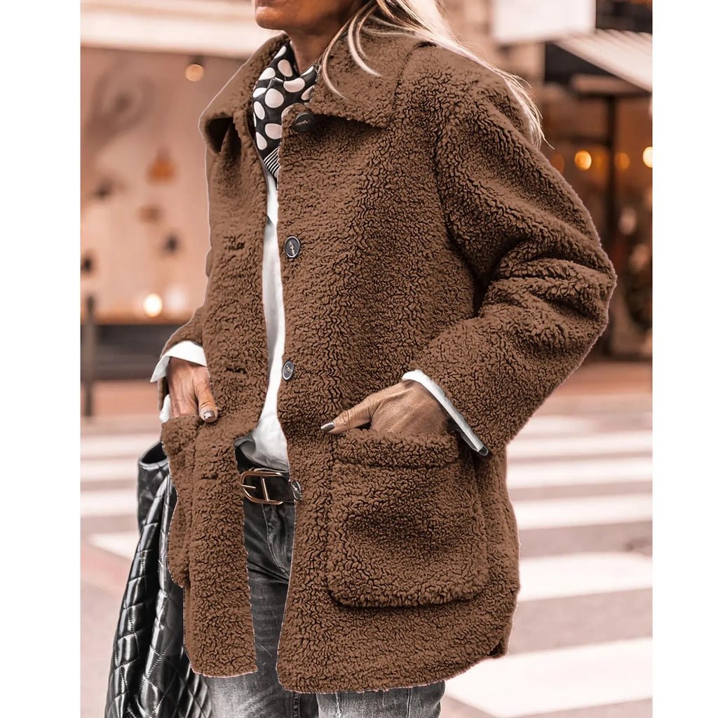 Femme portant un manteau en fausse fourrure marron, style décontracté, avec écharpe à pois, sur fond urbain. Mode automne-hiver tendance.
