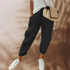Femme portant un pantalon noir ample, t-shirt blanc, baskets blanches et sac à bandoulière en paille. Mode décontractée, tendance et confortable.