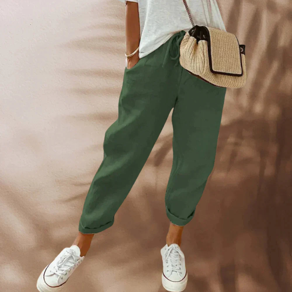 Pantalon vert décontracté pour femme, associé à un t-shirt blanc, baskets blanches et sac à bandoulière en paille. Mode estivale tendance.