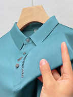 Polo bleu turquoise en tissu texturé, avec col boutonné et logo brodé "Gentle Polo", suspendu sur un cintre en bois.