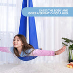 Fille souriante dans un hamac de yoga bleu, bras écartés, dans un salon lumineux. Texte: "Eases the body and gives a sensation of a hug".