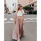 Femme élégante en jupe plissée rose et haut blanc, marchant en ville. Mode urbaine chic, style décontracté, lunettes de soleil, sac à main beige.