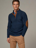Homme portant un pull bleu marine avec coudières marron et un pantalon beige. Mode masculine élégante, tenue automne-hiver, style décontracté.