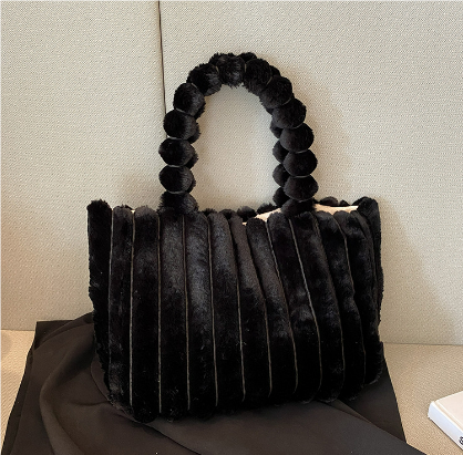 Sac à main en fausse fourrure noire avec anses perlées, posé sur un canapé beige. Accessoire mode élégant et tendance pour femme.