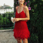 Robe rouge à franges portée par une femme souriante, tenant un sac à main transparent, devant un jardin fleuri. Mode élégante, soirée estivale.
