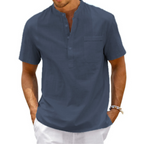 Homme portant une chemise bleue à col mao et manches courtes, avec un pantalon blanc. Mode estivale décontractée, style élégant et moderne.