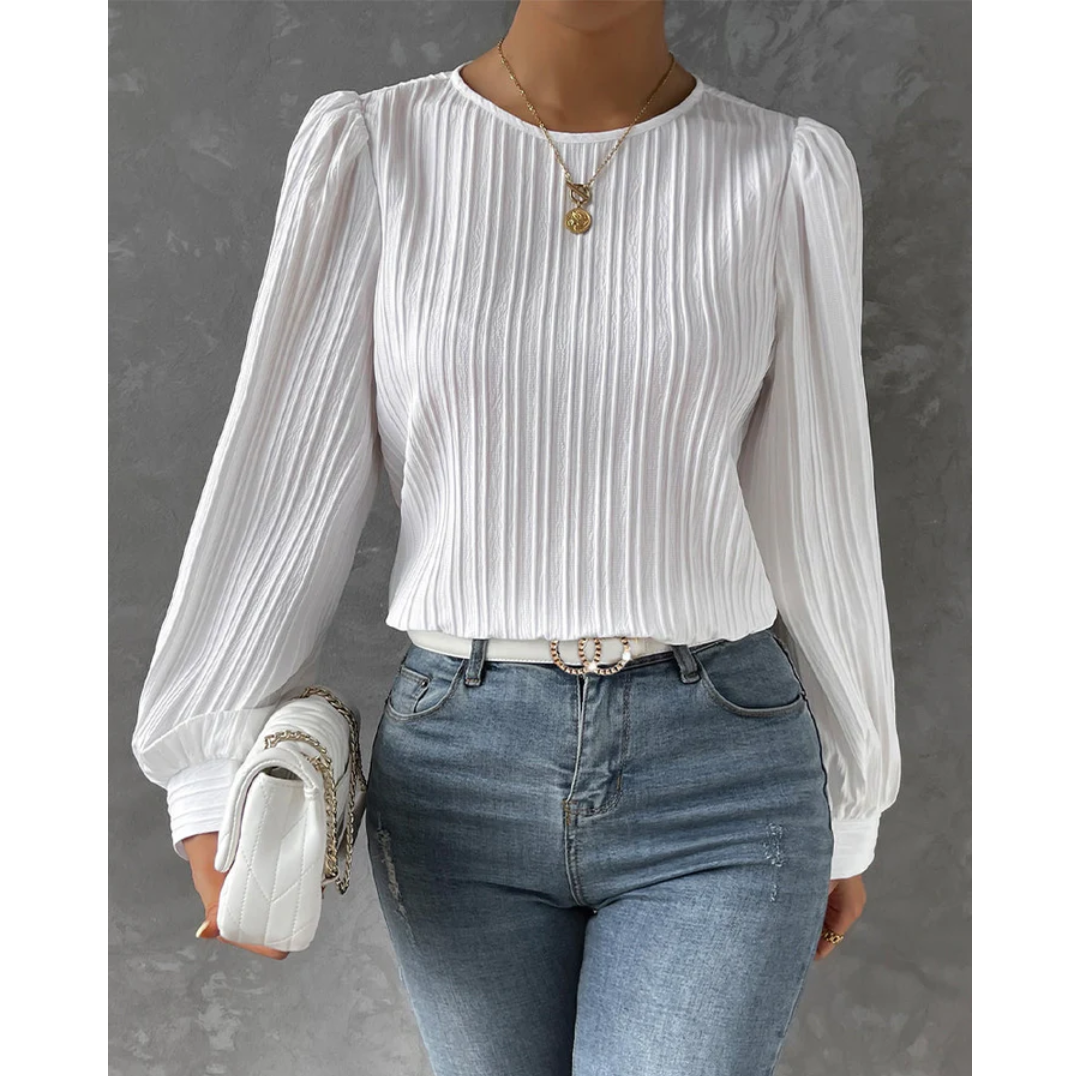 Femme portant un chemisier blanc à manches longues plissées, avec un jean bleu ajusté et un sac à main blanc. Mode élégante et tendance.