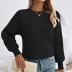 Femme portant un pull noir en tricot, jeans bleu, collier doré, tenant un sac à main beige. Mode automne-hiver, style décontracté chic.