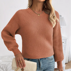 Femme portant un pull en maille marron, jeans bleu, tenant un sac à main beige. Mode automne, style décontracté, accessoires élégants.