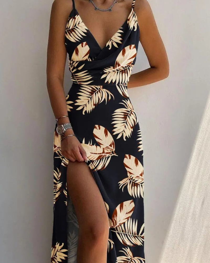 Robe longue noire à motifs tropicaux, fendue sur le côté, portée par une femme. Mode estivale élégante, tendance et chic.