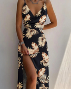 Robe longue noire à motifs tropicaux, fendue sur le côté, portée par une femme. Mode estivale élégante, tendance et chic.