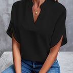 Blouse noire élégante avec col en V, manches courtes, portée par une femme assise en jean. Mode féminine chic, tenue décontractée tendance.
