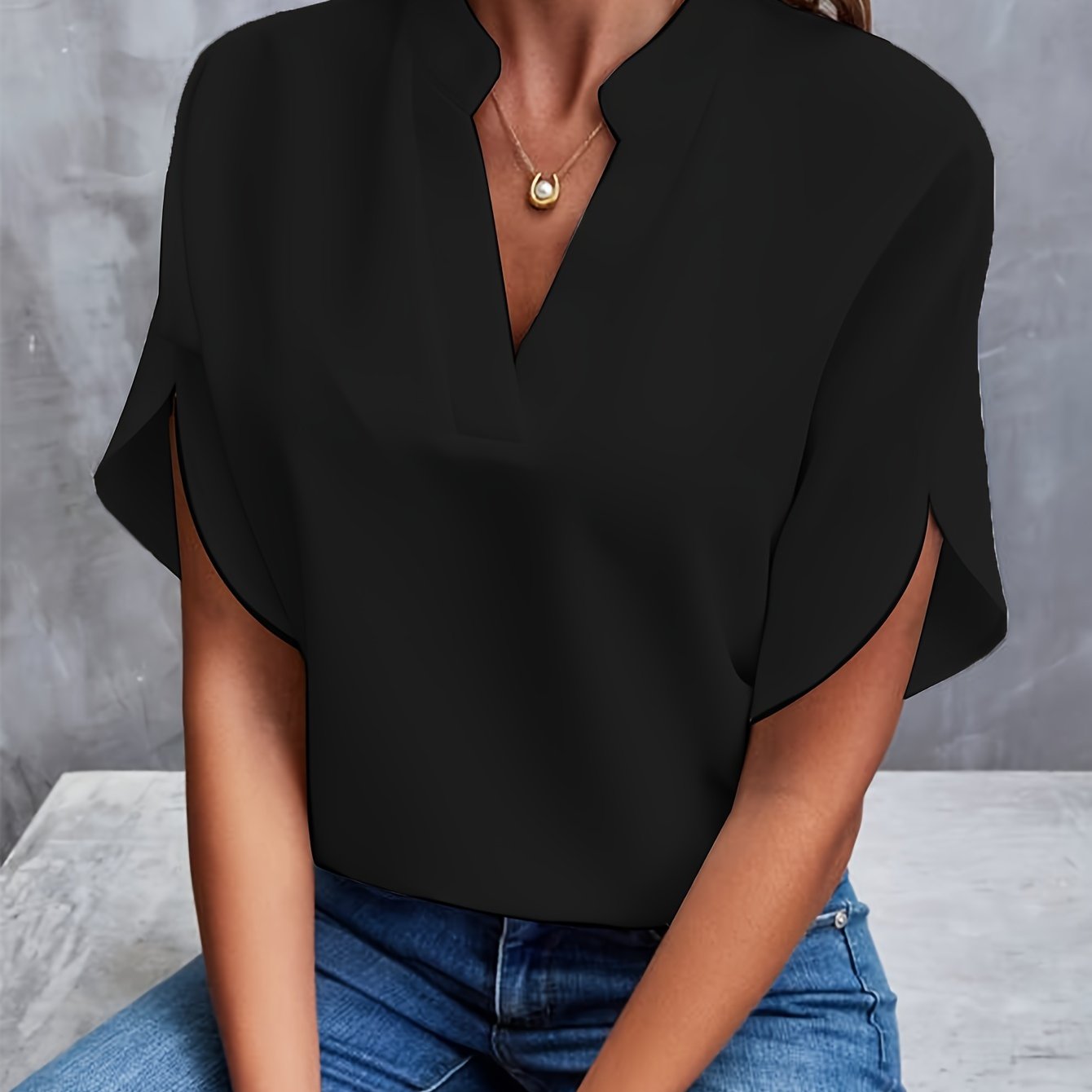 Blouse noire élégante avec col en V, manches courtes, portée par une femme assise en jean. Mode féminine chic, tenue décontractée tendance.